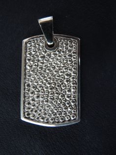 a dog tag is shown on a black leather surface, with silver dots all over it