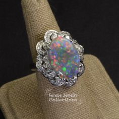 This remarkable Platinum Vintage Ring features a rare large black opal as its center piece. This specimen has a very even medium sized splashes of bright reds blues and greens play-of-color! The black opal is surrounded by a fancy floral like diamond pattern designs. Ring Size: 6.25 Total Weight: 15.75 grams Face Size: 1.1 inch x 0.9 inch Precious Metal: Platinum Precious stones: -Black Opal Center Stone: 6.17 carats, 18.1mm x 13.1mm -White Round Diamonds 0.78 carats Hallmark: Pt900 6.17 D0.78 Formal Multicolor Opal Ring, Elegant Multicolor Cabochon Opal Ring, Multicolor Oval Opal Ring For Formal Occasions, Unique Multi-stone Oval Opal Ring, Oval Opal Jewelry Collectible, Formal Multicolor Opal Gemstone Ring, Multicolor Opal Jewelry For Anniversary, Collectible Oval Opal Jewelry, Elegant Oval Untreated Opal Ring