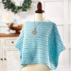 a blue crocheted shawl on a mannequin with a candle in the background