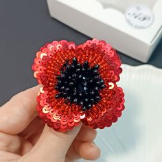 a red and black flower brooch sitting on top of a white plate next to a box