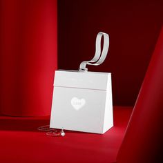 a white gift bag with a ribbon tied around it on a red surface next to a pair of scissors