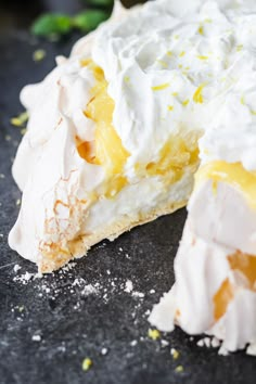 a piece of lemon meringue pie on a black surface with one slice missing