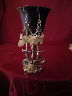 Coyote atlas vertebrae earrings with dangling sword. Available in gold or silver chains Available in shepherd's hooks or leverback hooks Due to the bones being real, they will slightly vary in size and color on each pair Bones are scrubbed with soap and water and cleaned with peroxide.  We do not use bleach or anything else that will weaken them Bone Colored Metal Earrings For Pierced Ears, Unique Bone-colored Nickel-free Earrings, Nickel-free Bone Dangle Earrings, Nickel-free Bone-colored Dangle Earrings, Nickel Free Bone Color Dangle Earrings, Symbolic Dangle Plug Earrings For Pierced Ears, White Gothic Handmade Earrings, Handmade White Gothic Earrings, Atlas Vertebrae