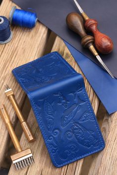 a blue leather case sitting on top of a wooden table next to scissors and thread