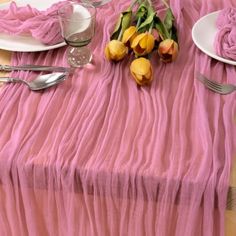 the table is set with plates, silverware and pink chiffon napkins