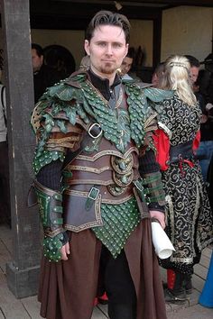 a man dressed in costume standing on a wooden deck with other people around him and looking at the camera