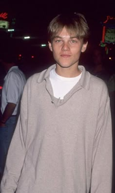 a young man standing in front of a crowd at night wearing a gray sweater and jeans