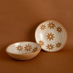 two brown and white bowls sitting next to each other on a brown tableclothed surface