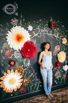 a woman standing in front of a chalkboard with flowers painted on it and the words,