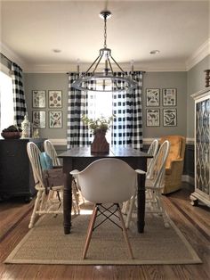 a dining room table with white chairs and black and white curtains on the windowsill