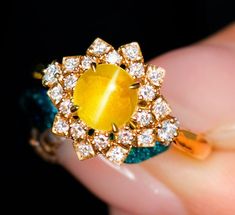 a close up of a person's hand holding a ring with an orange stone in it