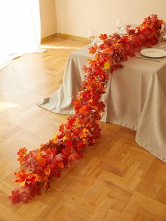 the table is set with white linens and red leaves on it, along with plates and silverware