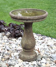 a stone bird bath sitting on top of a gravel bed next to a green lawn