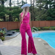 a woman standing in front of a pool wearing bright pink pants and a white hat