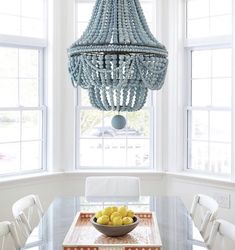 a dining room table with a bowl of lemons on it and a chandelier hanging from the ceiling