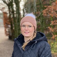 a woman wearing a hat and jacket standing in front of trees