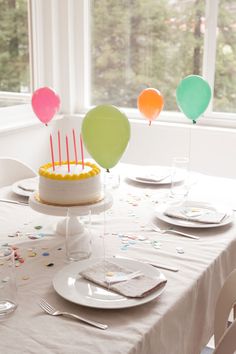 a birthday cake sitting on top of a table with balloons in the air above it