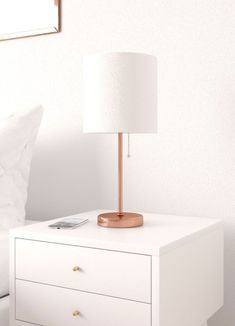 a nightstand with a lamp on top of it next to a white bed in a bedroom