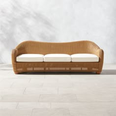 a wicker couch with white cushions on a tile floor in front of a wall