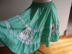 "This is a very cute 1960s vintage green cotton blend square dance full circle skirt. The skirt is made of a nice cotton and poly blend fabric with white lace ruffles and square cotton eyelet detail side pockets trimmed in gold rickrack. It has small, embroidered cactus and horseshoes on the white eyelet detail pockets. It slips on over the head with a wide elastic waist band and has no closures or fasteners. It was made by Pete Bettina, USA and the older size tag states size small. The measurements are as follows: Elastic Waist Band: 2\" wide Waist: 26\" relaxed to 29.5\" stretched Hips: Full Length: 23\" Condition: Very good condition with no obvious flaws or defects to note." Vintage Green Tiered Skirt, Green Full Cotton Skirt, Green Full Skirt With Ruffles, Retro Cotton Skirt With Ruffles, Fitted Green Petticoat For Spring, Embroidered Cactus, Square Dance, Full Circle Skirt, Green Square