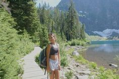 a woman standing on a path next to a body of water with trees in the background