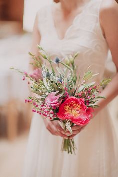 a woman in a white dress holding a pink flower and greenery bouquet on her wedding day