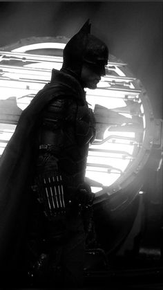 the dark knight is standing in front of a round window with light coming through it