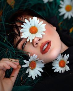 a woman laying in the grass with daisies on her face