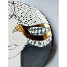 a white and gold plate with a bird on it's face in front of a gray background