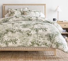 a bed with green and white comforter on top of it next to a night stand