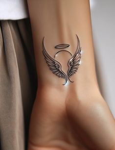 a woman's foot with an angel wing tattoo on her left side and the moon behind it