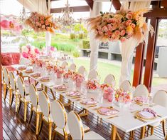 a long table set up with pink and white flowers, gold chairs and chandeliers