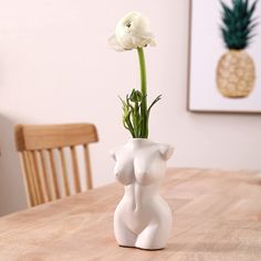 a white vase sitting on top of a wooden table next to a pineapple plant