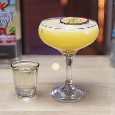 a yellow drink sitting on top of a table next to a glass filled with liquid