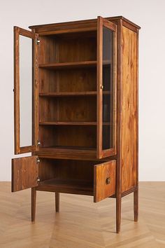 a wooden cabinet with its doors open on top of a hard wood floor next to a mirror