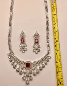 Add elegance to any outfit with our CZ American Diamond Necklace. The sparkling ruby stones add a touch of glamour, making it perfect for any occasion. Our high-quality CZ stones provide the look of real diamonds without the high price tag. Elevate your style with our stunning necklace. This jewellery set includes a necklace and matching earrings. Jewellery Care- Keep the jewellery dry, avoid contact with perfumes and water. Luxury Ruby Diamond Necklace With Diamond Accents, Luxury Ruby Diamond Necklace With Accents, Luxury Ruby Necklaces With Diamond Accents, Luxury Ruby Necklace With Diamond Accents, Elegant Diamond Jewelry Sets With Rhinestones, Diamond White Ruby Necklace With 17 Jewels, Red Diamond Cut Necklace For Formal Occasions, Dazzling Ruby Necklace With Diamond Cut, Red Diamond Cut Necklace