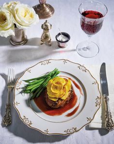 a white plate topped with food next to a glass of wine and two silver spoons