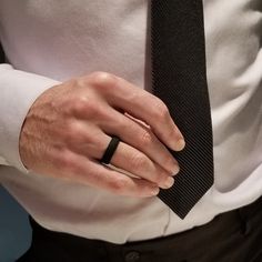 a man in a white shirt and black tie is wearing a ring on his left hand