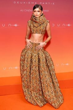 a woman standing in front of an orange and pink background wearing a dress with high slits