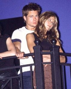 a man and woman standing next to each other on top of a metal balcony railing