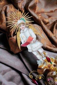 an angel doll is sitting next to a christmas tree ornament on a bed