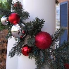 a white pillar decorated with red and silver christmas balls, pine branches and ornaments hanging from it