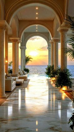 an indoor swimming pool surrounded by columns and potted plants with the sun setting in the background