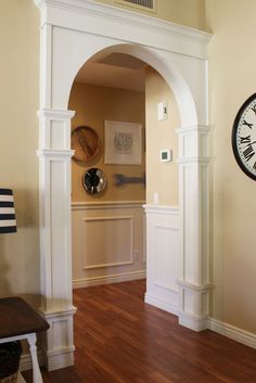 an archway leading into a living room with a clock on the wall and wooden floors