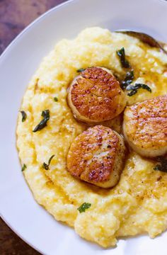 a white plate topped with mashed potatoes and seared scallops on top of grits