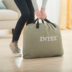 a person holding onto a bag with the word intex printed on it while standing in front of a couch