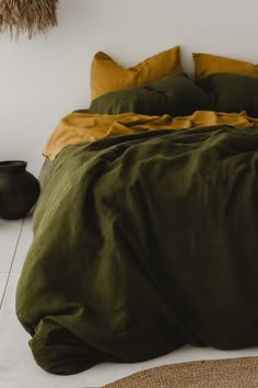 a bed with green sheets and pillows in a room next to a rug on the floor