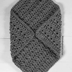 a gray crocheted neck tie laying on top of a white wall