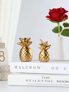 two gold pineapple bookends sitting on top of a stack of books next to a red rose