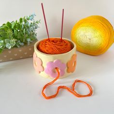 yarn and knitting needles in a bowl next to a plant